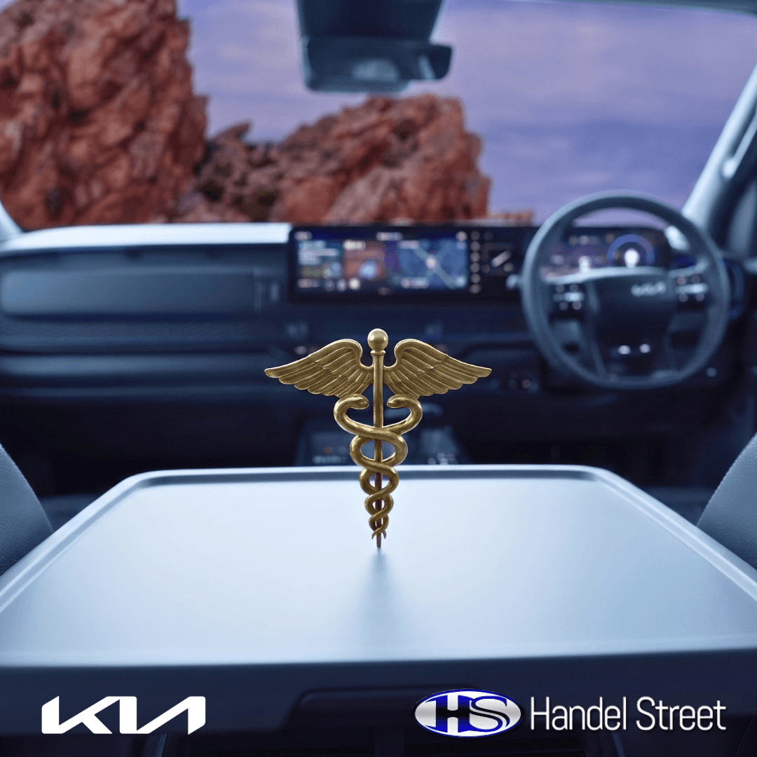 A gold medical caduceus emblem rests on the flat center console table inside the custom cabin of a Kia Tasman, showcasing the modern digital dashboard and steering wheel design by Handel Street. kia-tasman-medical-fleet-interior-handel-street.jpg